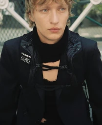 Portrait of a blonde male model wearing a black jacket and branded collar for MM6 Maison Margiela x Salomon.