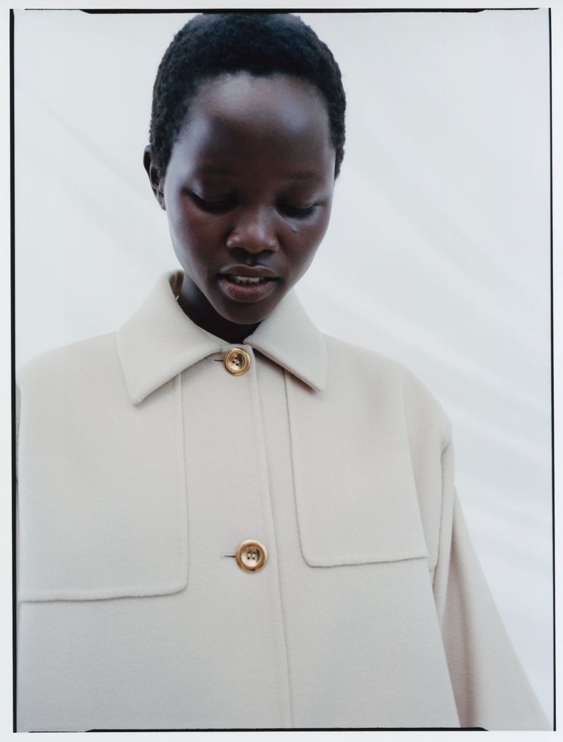 Close-up portrait of a model wearing a cream-colored buttoned coat against a light neutral background.