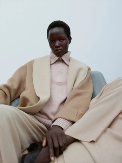 Elegant dark-skinned woman in tailored separates. Sitting with legs crossed, looking intently into the camera, style and poise.