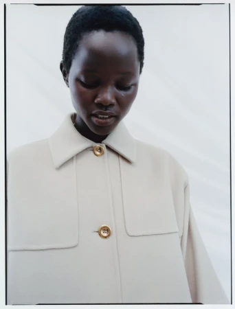 Close-up portrait of a model wearing a cream-colored buttoned coat against a light neutral background.