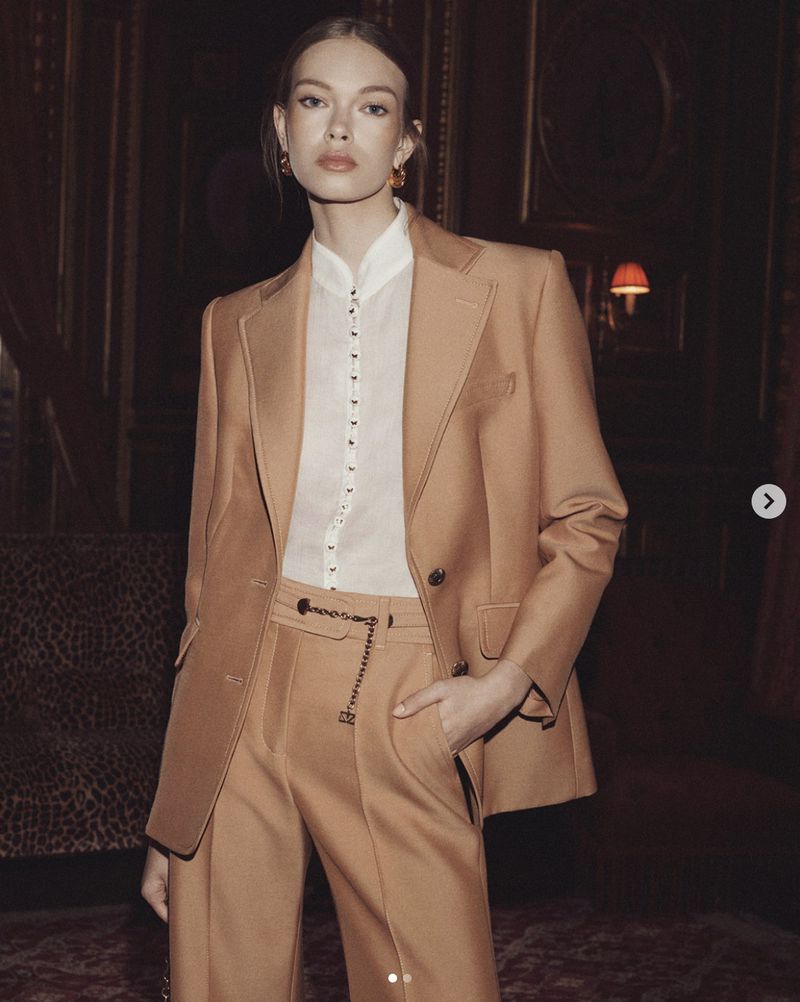 Model wearing a camel suit jacket and trousers with a white button-up shirt in an interior setting