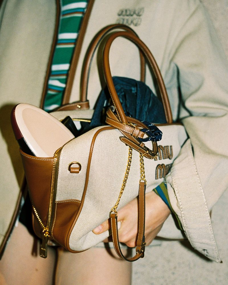 Cream and brown Miu Miu handbag held by a person wearing a beige jacket, showcasing fashion accessory and modern style.