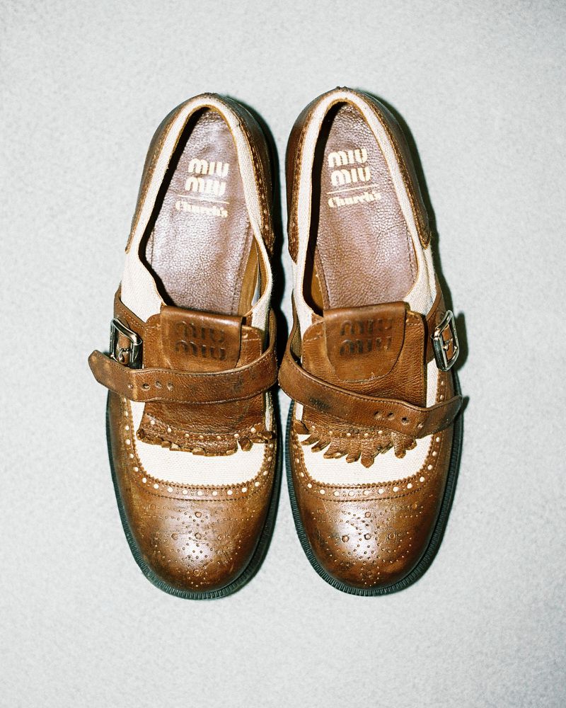 Elevated shot of brown leather Miu Miu Mary Jane shoes. The shoes are displayed side-by-side against a solid light grey backdrop.