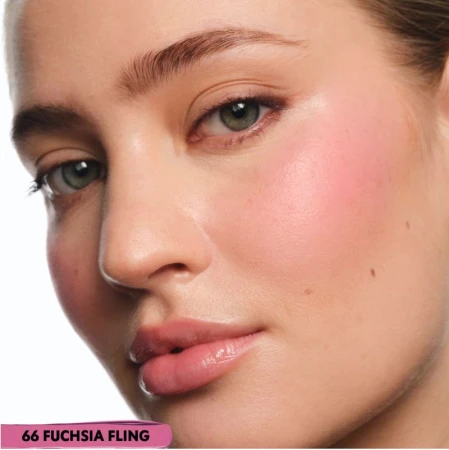 Close-up portrait of an adult woman with pink blush on her cheeks, full lips, and fair skin against a white background in a beauty context.