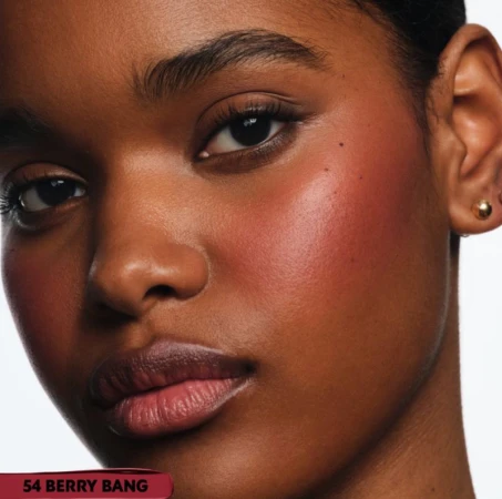 Close-up portrait of an adult woman with dark skin, makeup, and an earring, set against a clean, bright background.