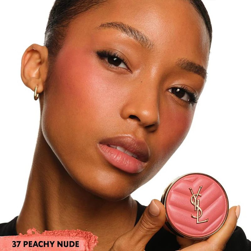 Close-up of a woman wearing blush and holding a compact of blush in her hand, showcasing makeup and beauty products.