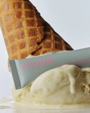 Close-up studio shot of an ice cream cone melting with a tube of skincare product, against a white background, product photography.