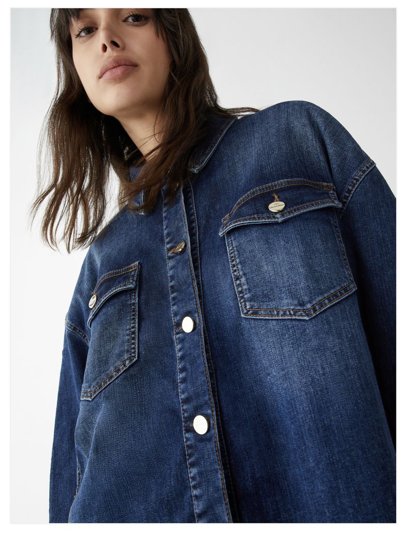 Brunette woman in a button-down denim shirt with chest pockets, photographed in a high-angle studio shot with a white background.