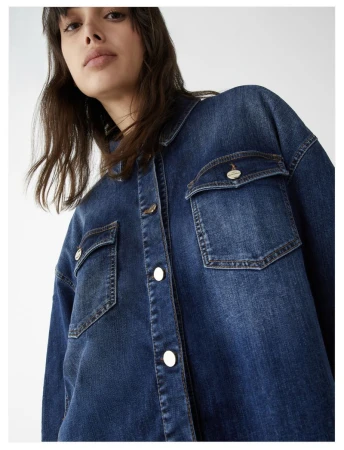 Brunette woman in a button-down denim shirt with chest pockets, photographed in a high-angle studio shot with a white background.