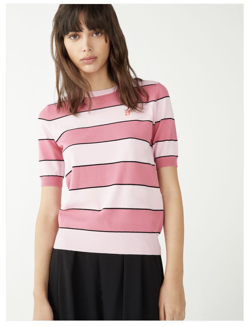 A woman poses in a pink and white striped short-sleeved shirt and black skirt against a white background in a studio shot.