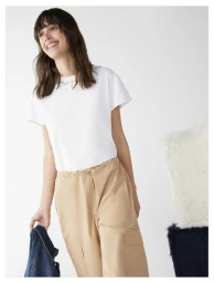 Rosa Kirakosyan wearing an embellished white t-shirt and beige cargo trousers while holding a denim jacket against a white backdrop.