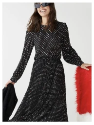 Smiling model wearing a black polka dot dress and sunglasses against a plain background for i Blues Summer 2024 collection.