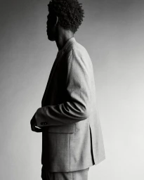 Black man wearing a tailored suit jacket in profile view against a neutral gradient studio background