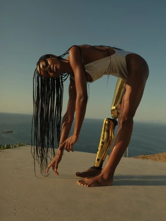 Athletic woman with a prosthetic leg bends over on an outdoor terrace against a blue sky and ocean, showcasing strength and resilience.