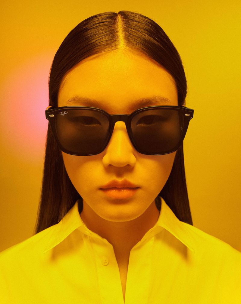 Headshot of an Asian female wearing sunglasses and a white shirt, illuminated by a warm, golden yellow light with a soft pink gradient.