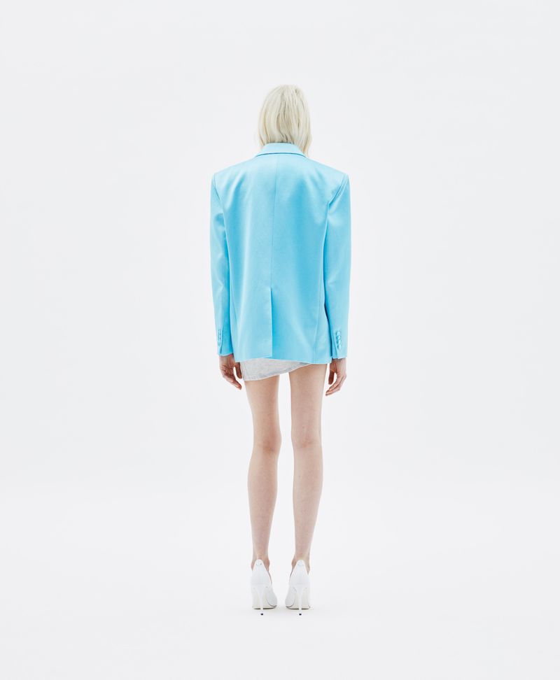 Model seen from behind wearing a light blue blazer and white heels against a plain white background