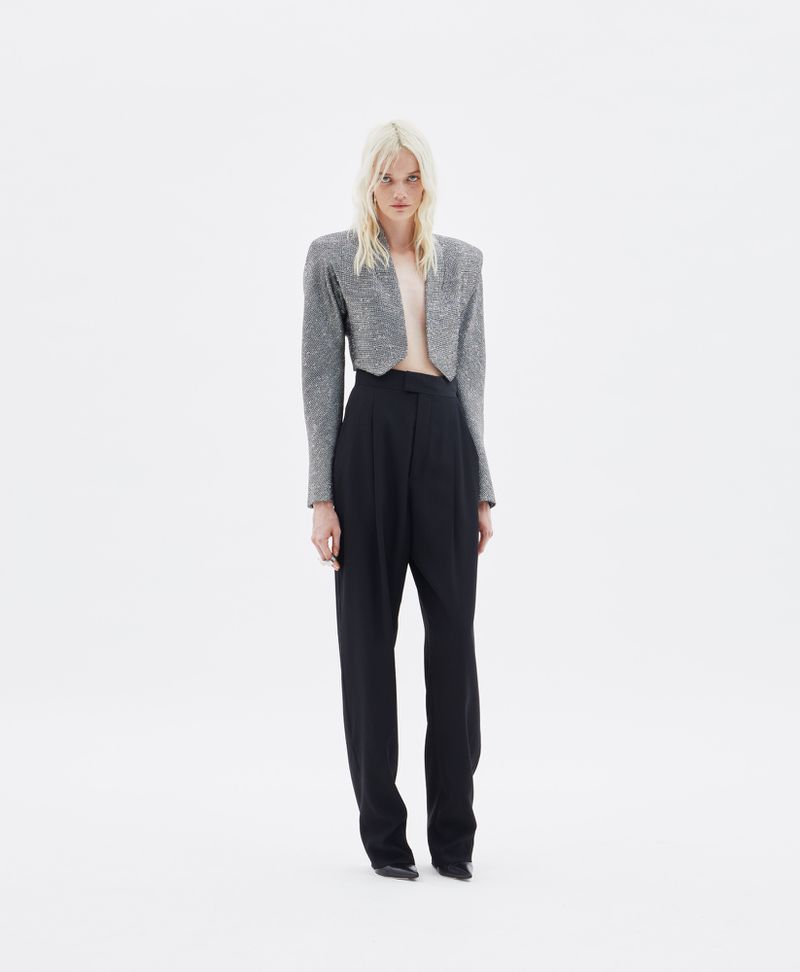 Model wearing a cropped grey embellished blazer and high-waisted black trousers against a plain white seamless backdrop