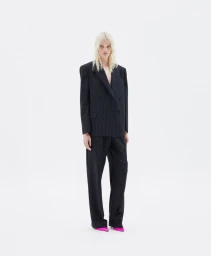 Model in a black pinstripe suit and bright pink shoes standing against a plain white background
