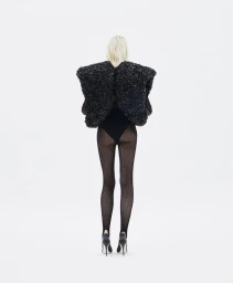 Model standing facing away from the camera wearing a black textured structured top and sheer black tights against a plain white background.