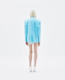 Model seen from behind wearing a light blue blazer and white heels against a plain white background