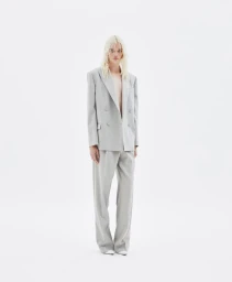Model wearing a grey double-breasted blazer and matching trousers against a white seamless background