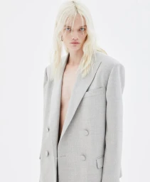 Model with blonde hair wearing a grey blazer against a plain white seamless studio background