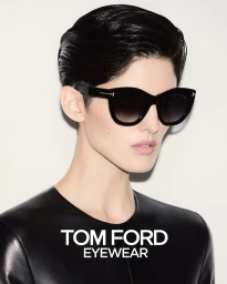Model with dark styled hair wearing black sunglasses and a black leather top against a neutral background.