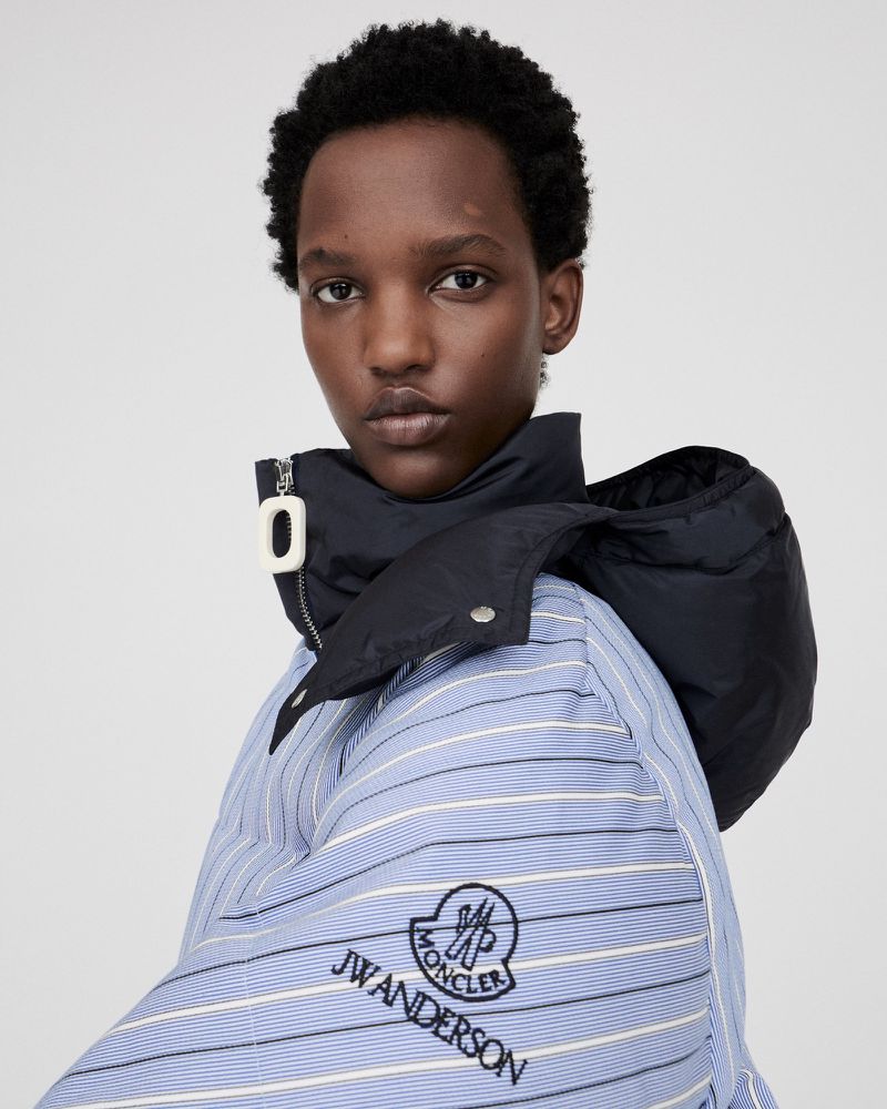 Adult female poses in a blue and white striped puffer jacket with a black hood, set against a neutral studio backdrop.