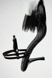 Black patent heeled sandal with sheer mesh bow detail against a white seamless studio background.