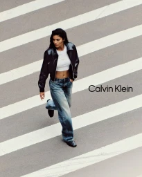 Model Rania Benchegra wearing a black leather jacket and denim jeans walking across a striped street for Calvin Klein Fall 2025 Denim.