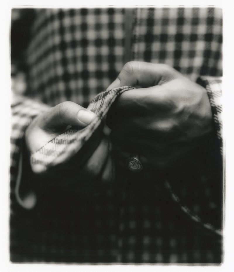 Close-up of hands holding checkered fabric, showing detailed texture and craftsmanship in a black and white photograph.