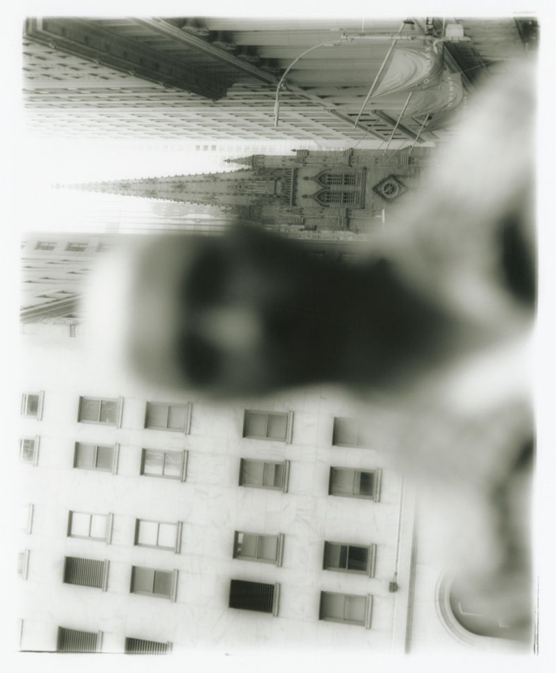 Monochrome urban view of a tall building with many windows and a church steeple extending above the roofline, giving a perspective from below.
