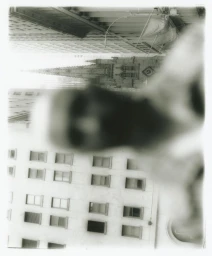 Heavily blurred silhouette of a person against urban architecture with repetitive windows and a distant spire.