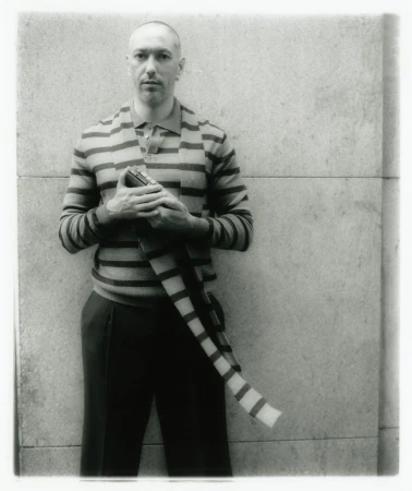 Portrait of a man wearing a striped cardigan standing against a stone wall background