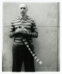 Portrait of a man wearing a striped cardigan standing against a stone wall background