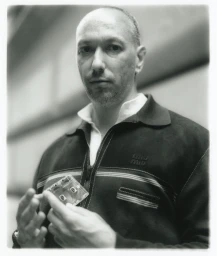 Portrait of a man holding a cassette tape wearing a zipped jacket for Present Space photographed by Javier Castan