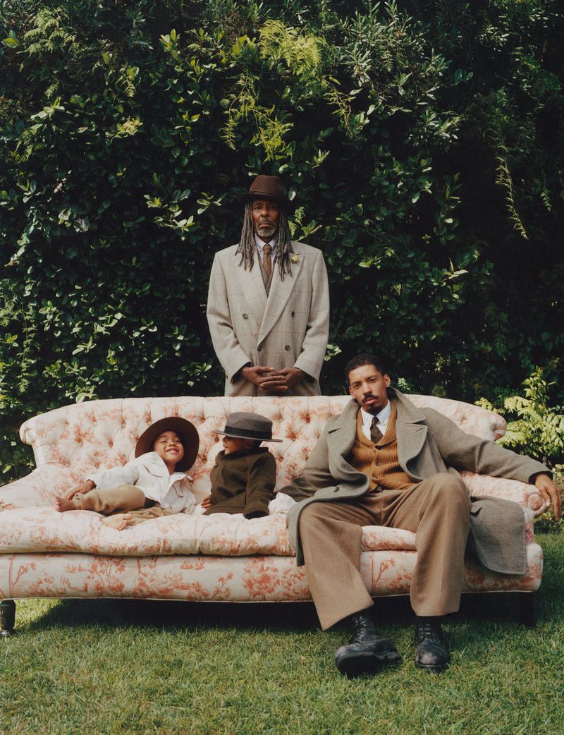 Two children and two adults on an ornate floral sofa in a garden setting. The group is dressed in warm layers and vintage attire.