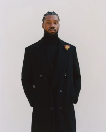 Portrait of a confident adult male of African descent wearing a black turtleneck sweater and a double-breasted wool coat in a studio.