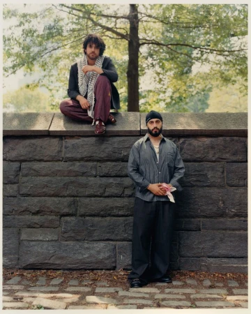 Two men posing outdoors against a dark stone wall with a tree behind them for an editorial feature in The Greatest Magazine.