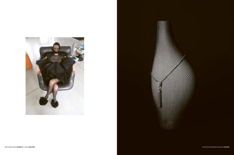 Woman in a black dress sits in a black chair and a dotted bag-shaped vase is against a black background in a studio setting.