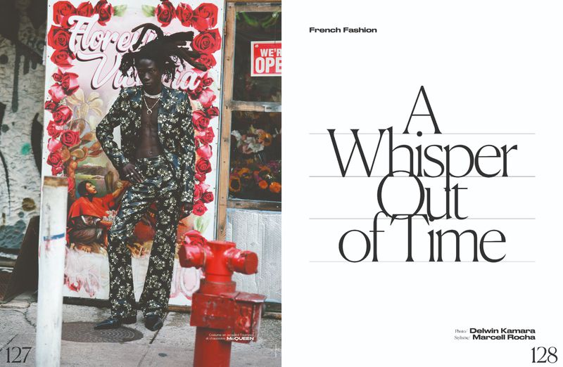 Fashion shot: An adult male model in a floral suit poses outdoors next to a floral wall, with a red fire hydrant in the foreground.