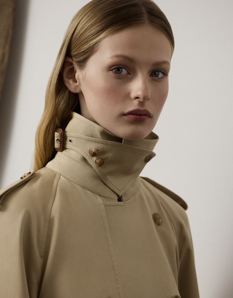 Blond woman in a tan trench coat. Close-up studio shot of a woman with fair skin, looking at the camera, wearing a beige coat.