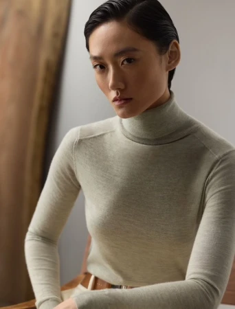 Model wearing a light grey turtleneck sweater with dark slicked-back hair against a neutral studio backdrop.