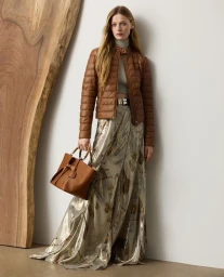 Model wearing a brown quilted leather jacket and metallic patterned skirt holding a tan leather handbag.