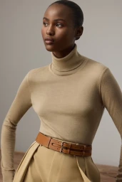 Model wearing a camel turtleneck sweater and tan trousers with a double-buckle leather belt against a neutral studio backdrop
