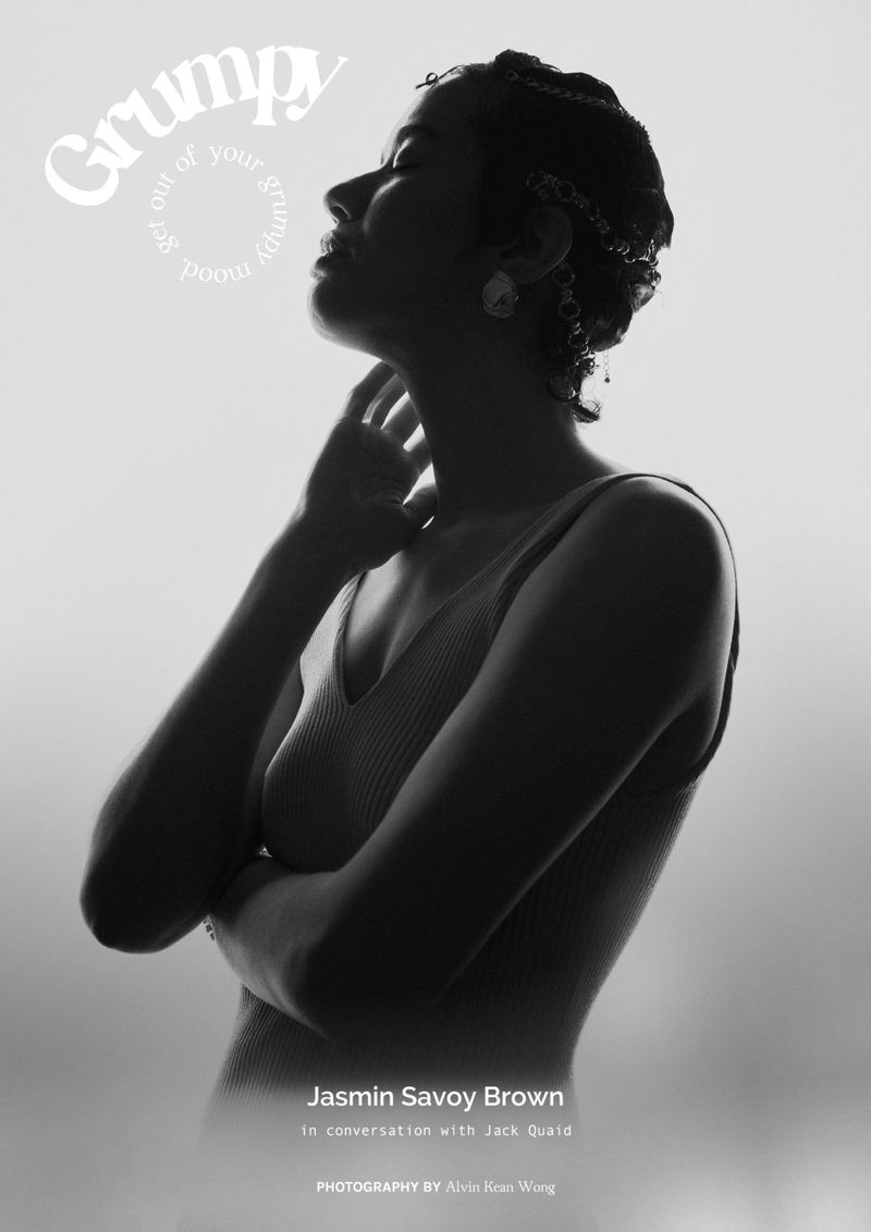 Monochromatic profile portrait of a woman in a tank top, posing with crossed arms and head tilted back in a bright, studio setting.