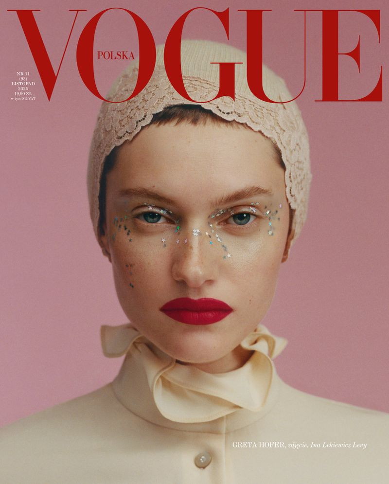 Close-up portrait of a woman wearing a lace bonnet with embellished eye makeup and red lipstick on a pink background, Vogue Polska cover.