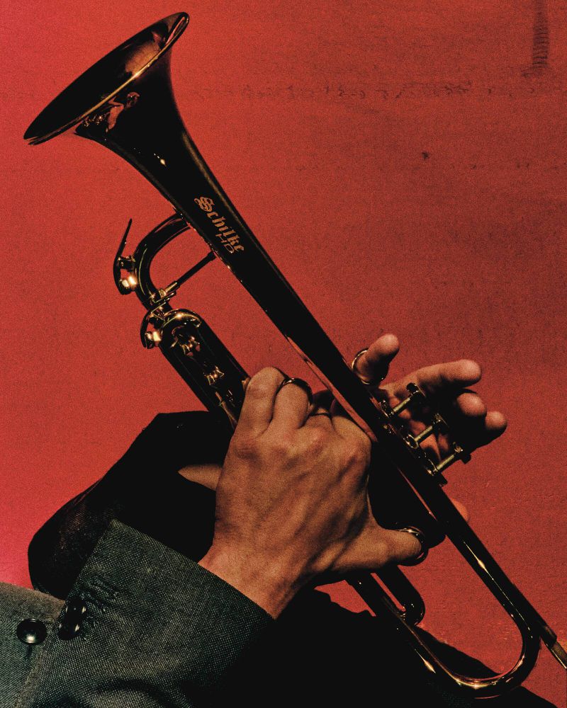 Close-up of a person playing a golden Schilke trumpet against a vibrant red backdrop, showcasing music and instrument detail.