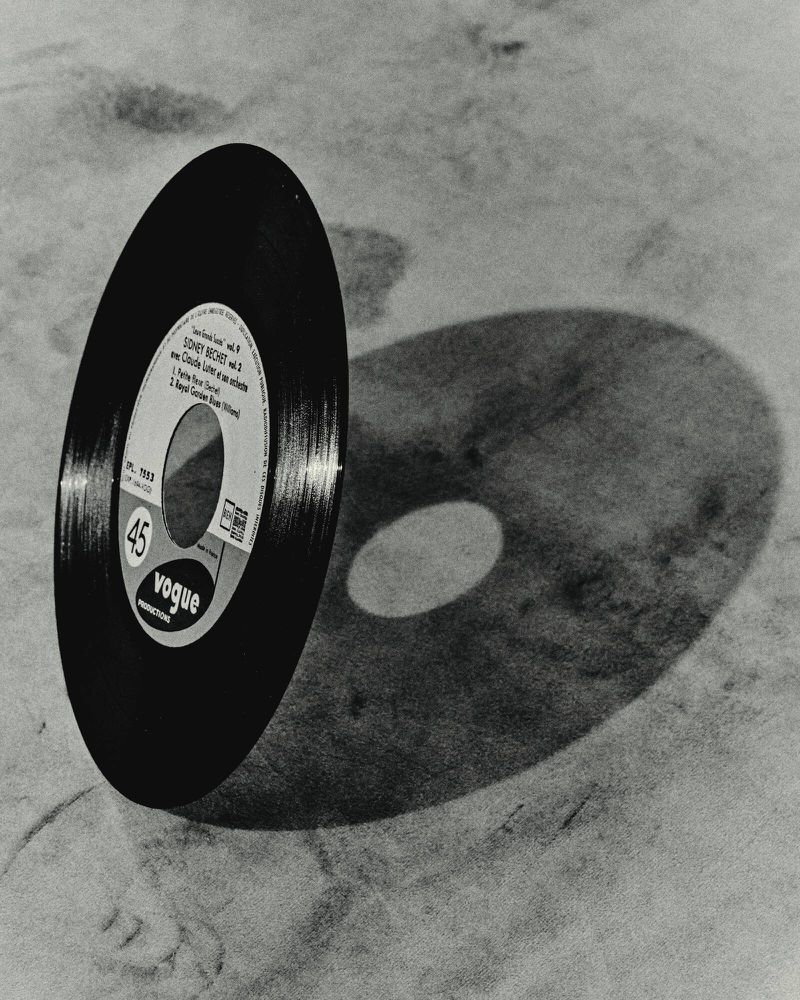 High-angle shot of a vintage Vogue 45 record casting a shadow, set against a textured neutral surface, showcasing retro music culture.