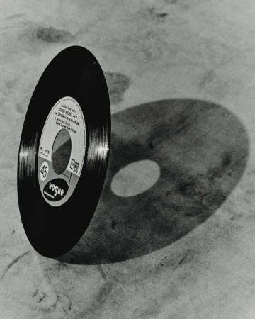 High-angle shot of a vintage Vogue 45 record casting a shadow, set against a textured neutral surface, showcasing retro music culture.